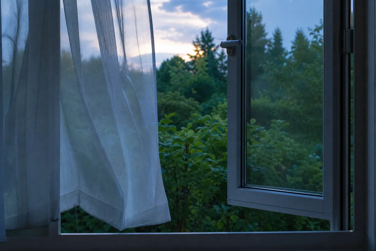 Fenêtre entrouverte au crépuscule sur un jardin, ambiance de nuit d’été fraîche